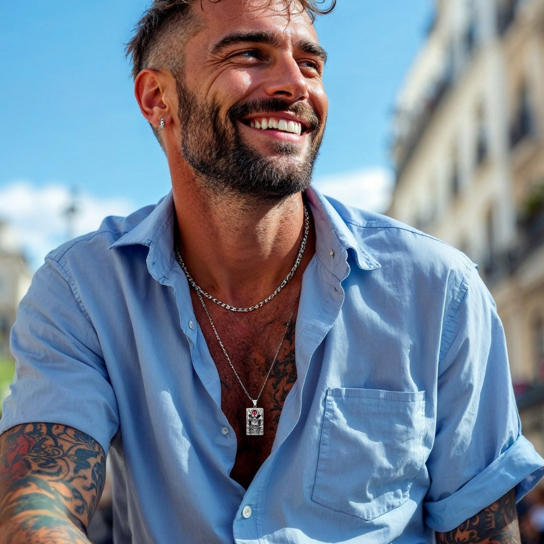 Collier homme- pendentif- tête de mort- skull- homme-élégant-chemise-bleue-pâle-tatouages-boucle-oreille-barbe-courte- assied- à- Paris