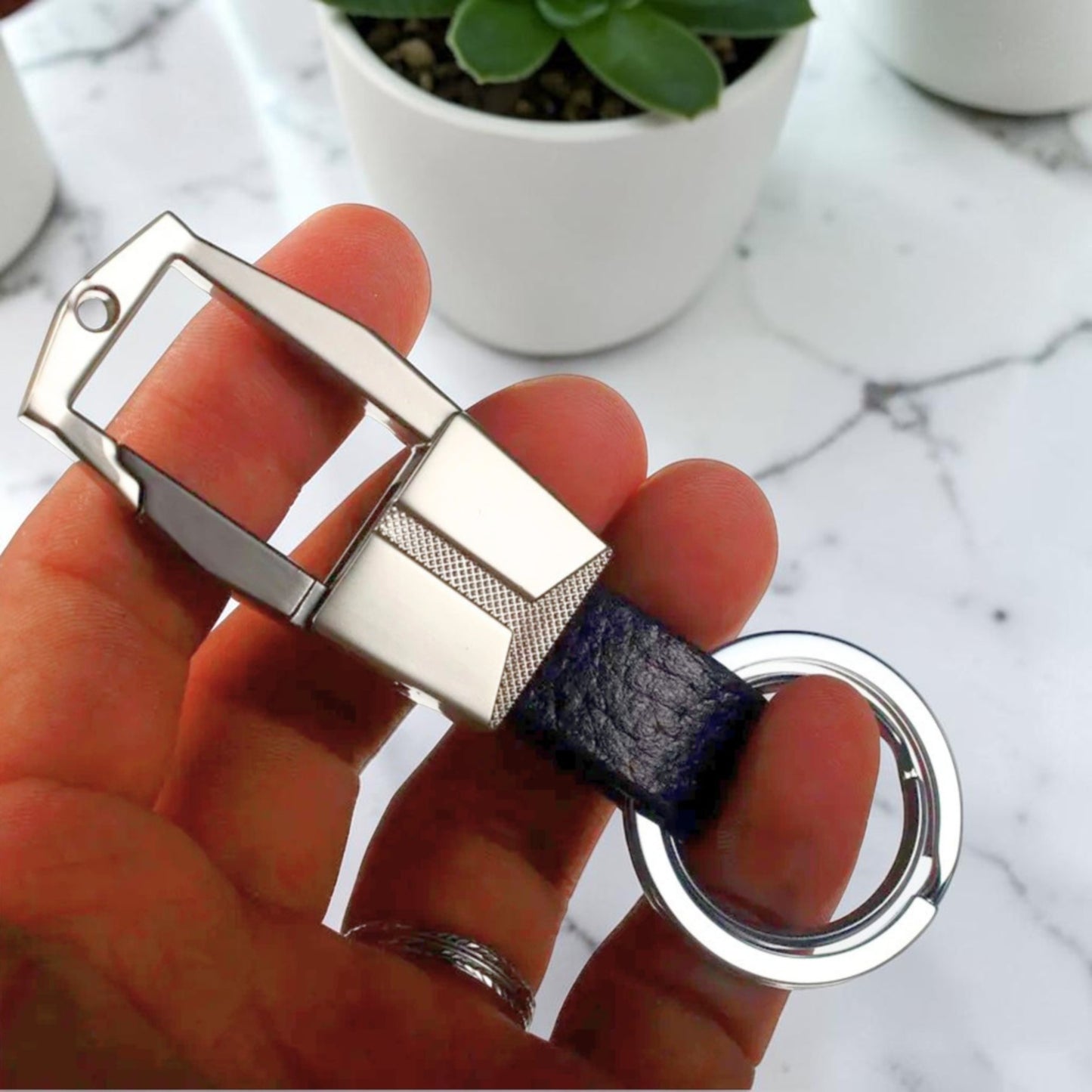 Mousqueton porte-clé métal argenté et cuir bleu marine tenu en main - finition guillochée mmihommesmodernes.com